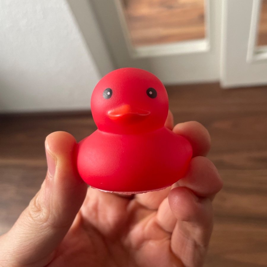 A red rubber duck held in a hand